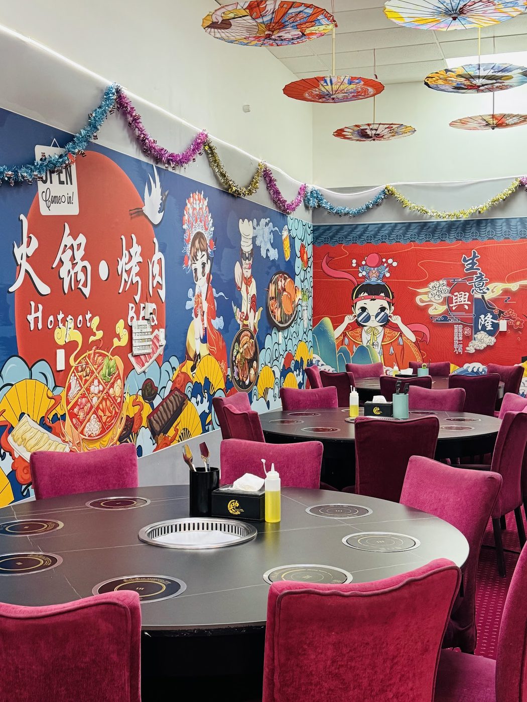 Round dining tables with built-in grills and induction rings, in front of a painted opera-mask wall